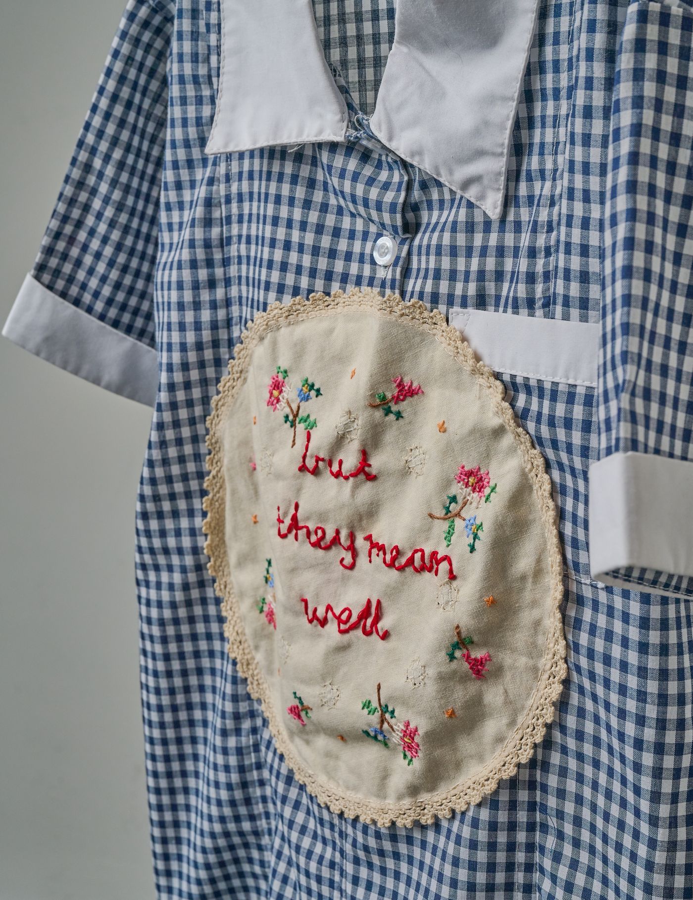 Detail — “but they mean well” embroidered in red thread on the napkin
