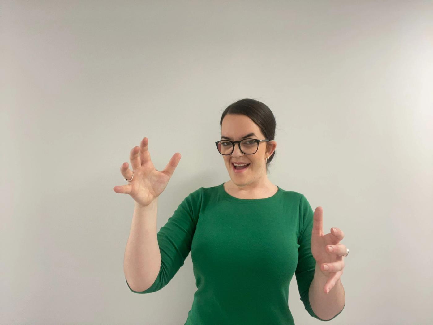 Catherine Dunn signing to camera in a green top against a white wall