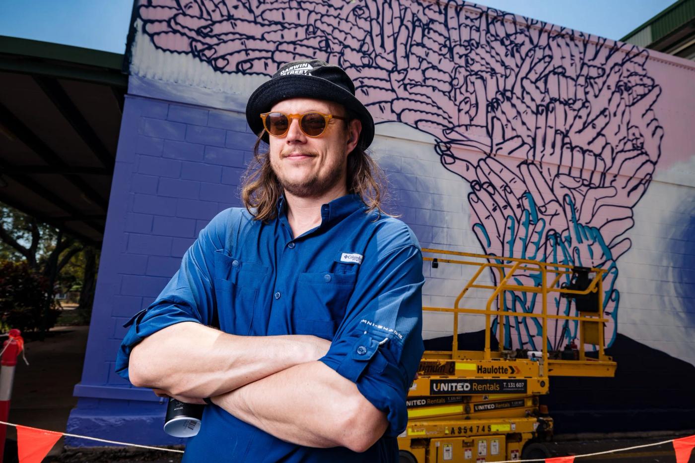 Gonketa in front of his mural of interlocking hands