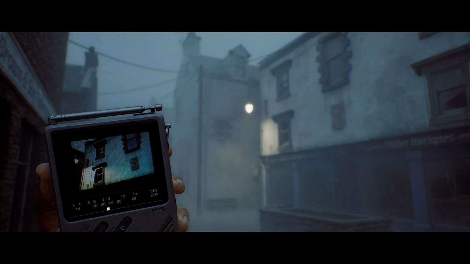 First-person view of a hand holding a small CRT television showing a building, on a foggy street