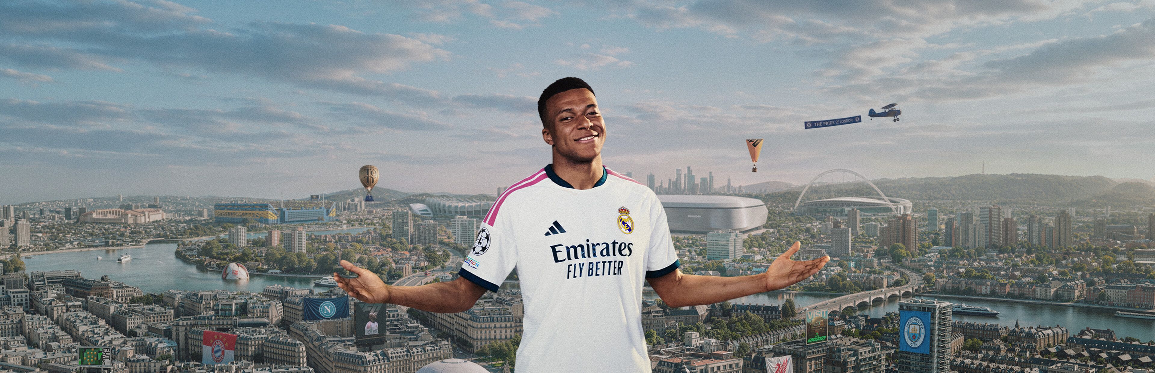A footballer in a white kit spreads his arms in front of a wide city skyline with stadiums and a river