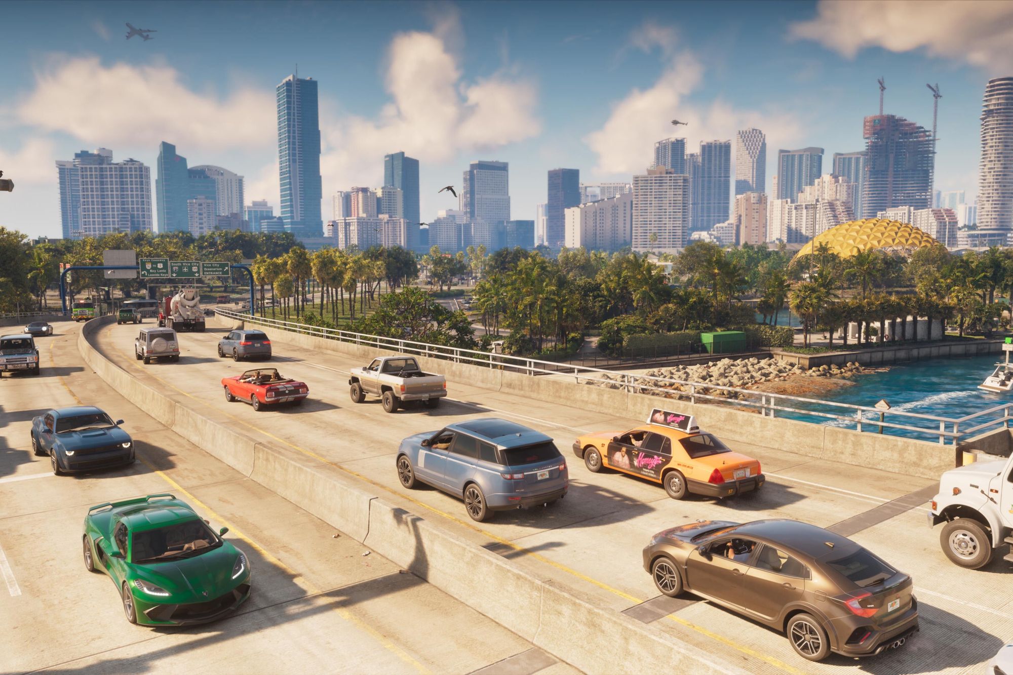 Cars and a taxi on a sunny Vice City highway with palm trees, the sea and a skyline of towers behind