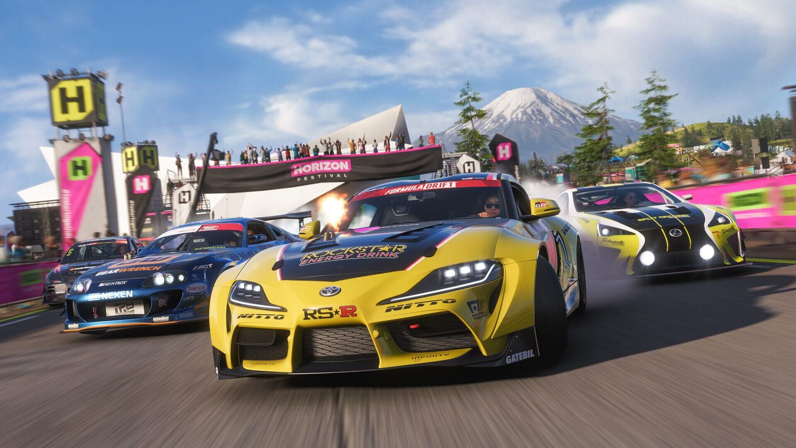 Race-liveried cars three-abreast past the Horizon Festival stage with a volcano behind