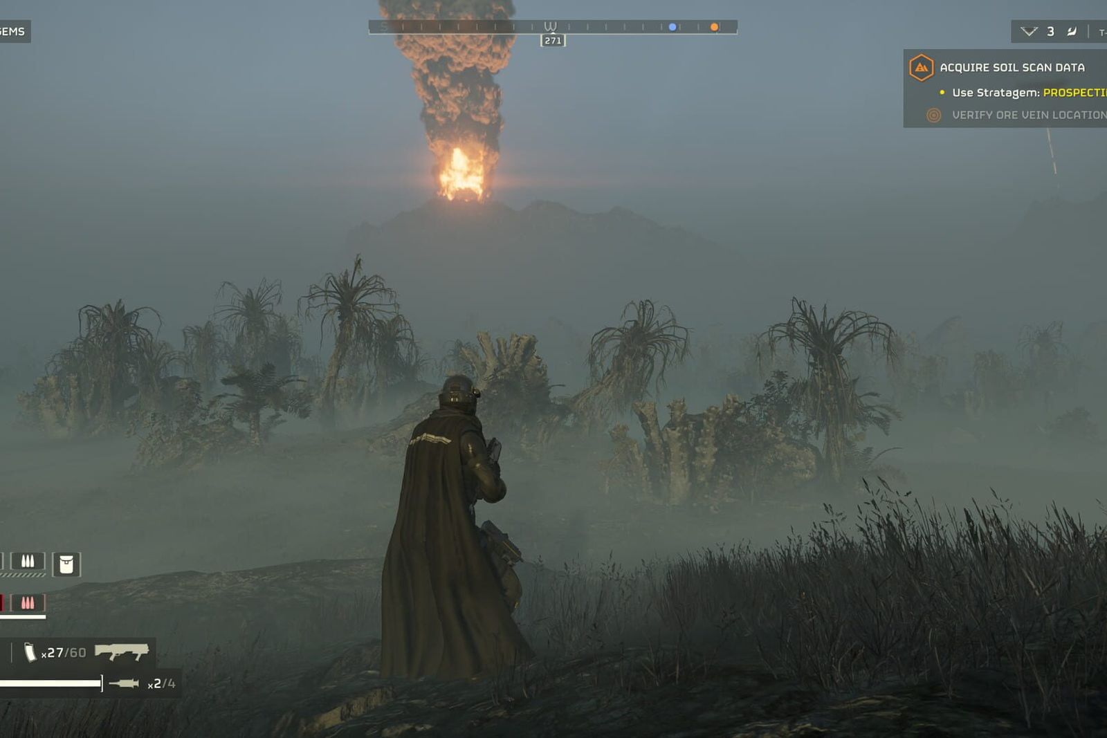 A Helldiver in a long coat stands in foggy jungle grass as a column of fire and smoke rises in the distance.