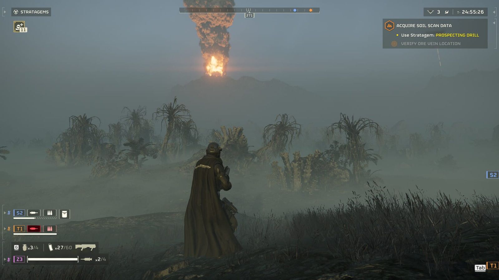 A Helldiver in a long coat stands in foggy jungle grass as a column of fire and smoke rises in the distance.