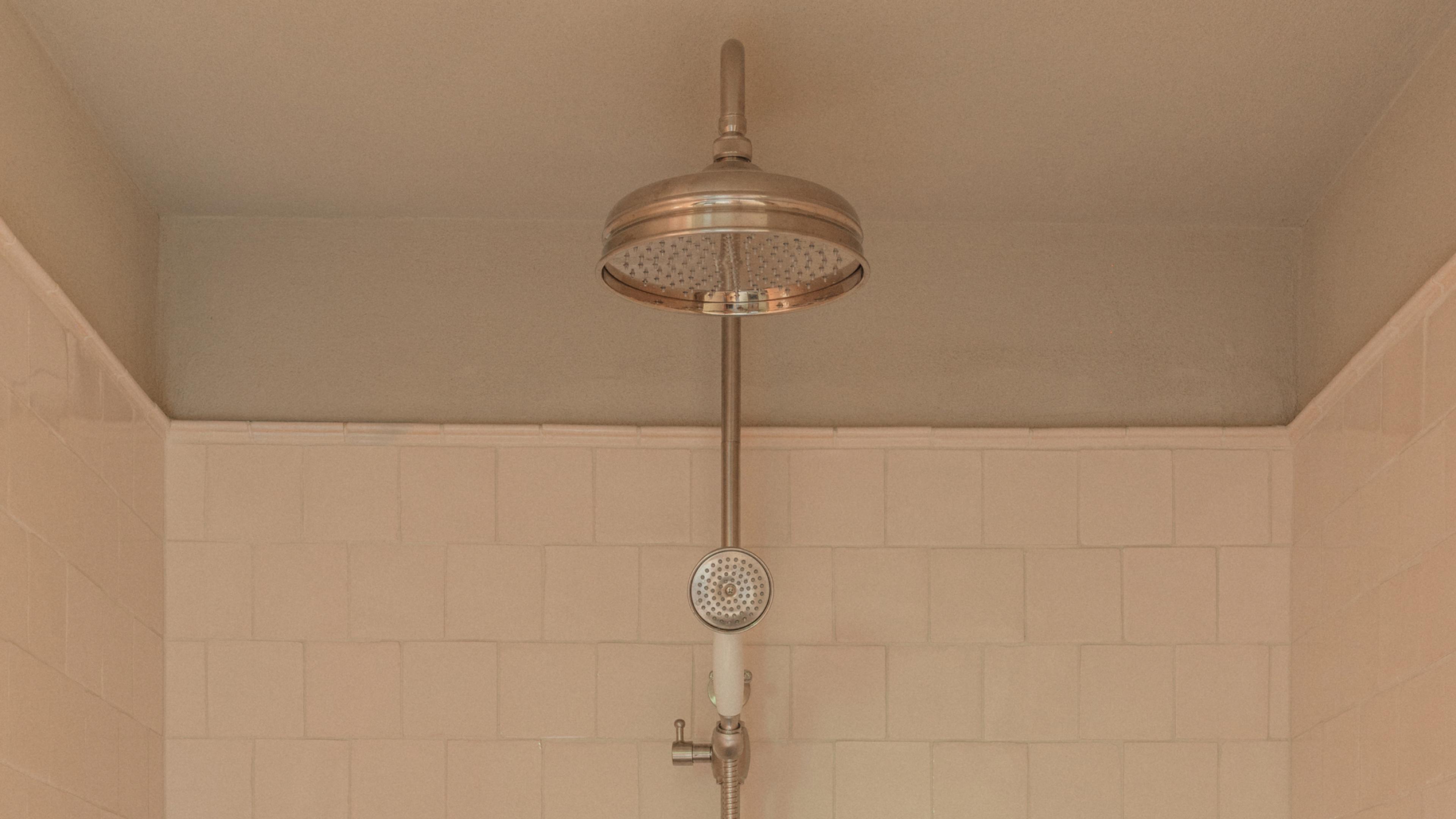 Nickel-finish shower set with a round rain head and a handheld spray on a riser rail, against cream square tiles