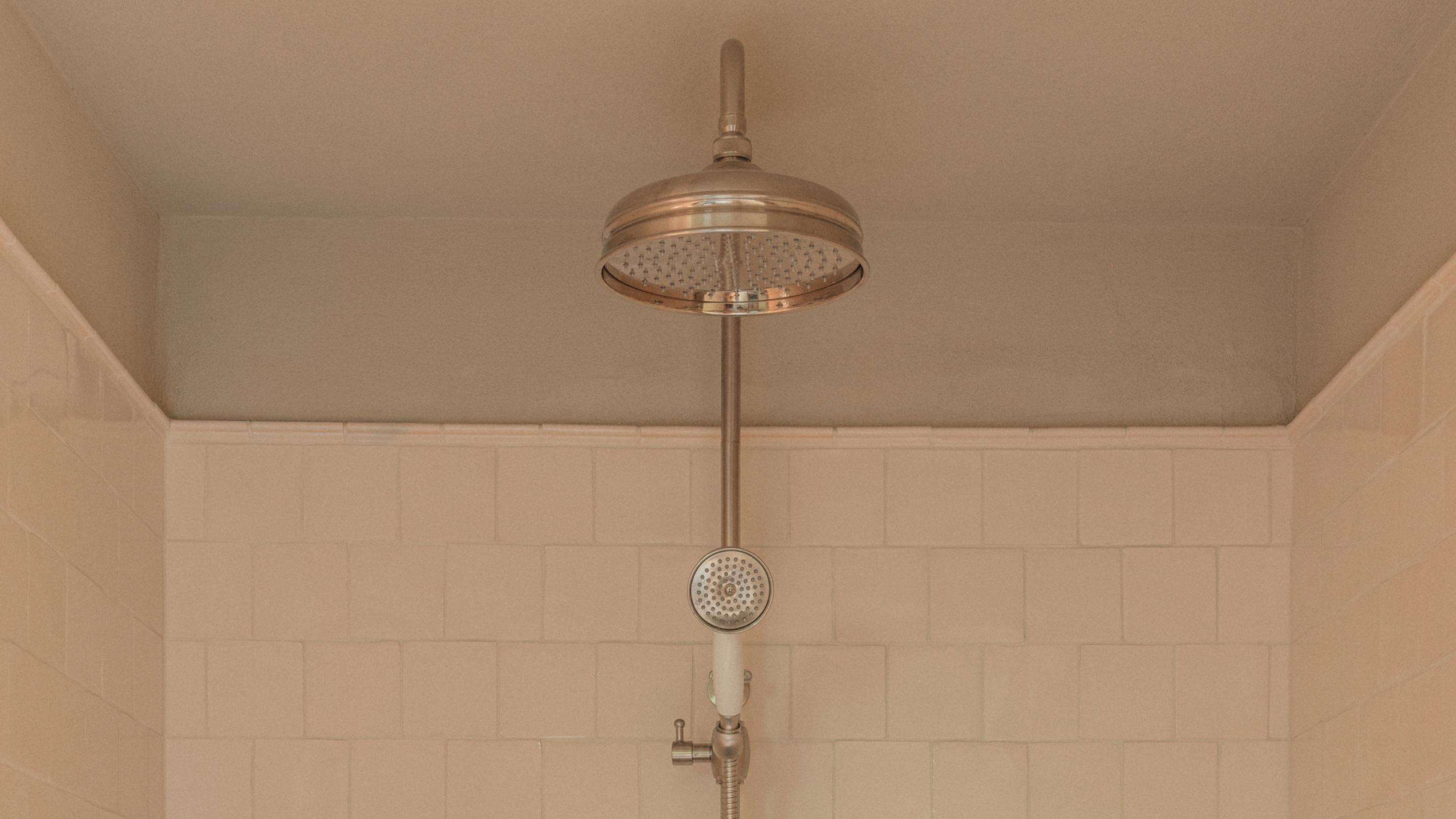 Nickel-finish shower set with a round rain head and a handheld spray on a riser rail, against cream square tiles