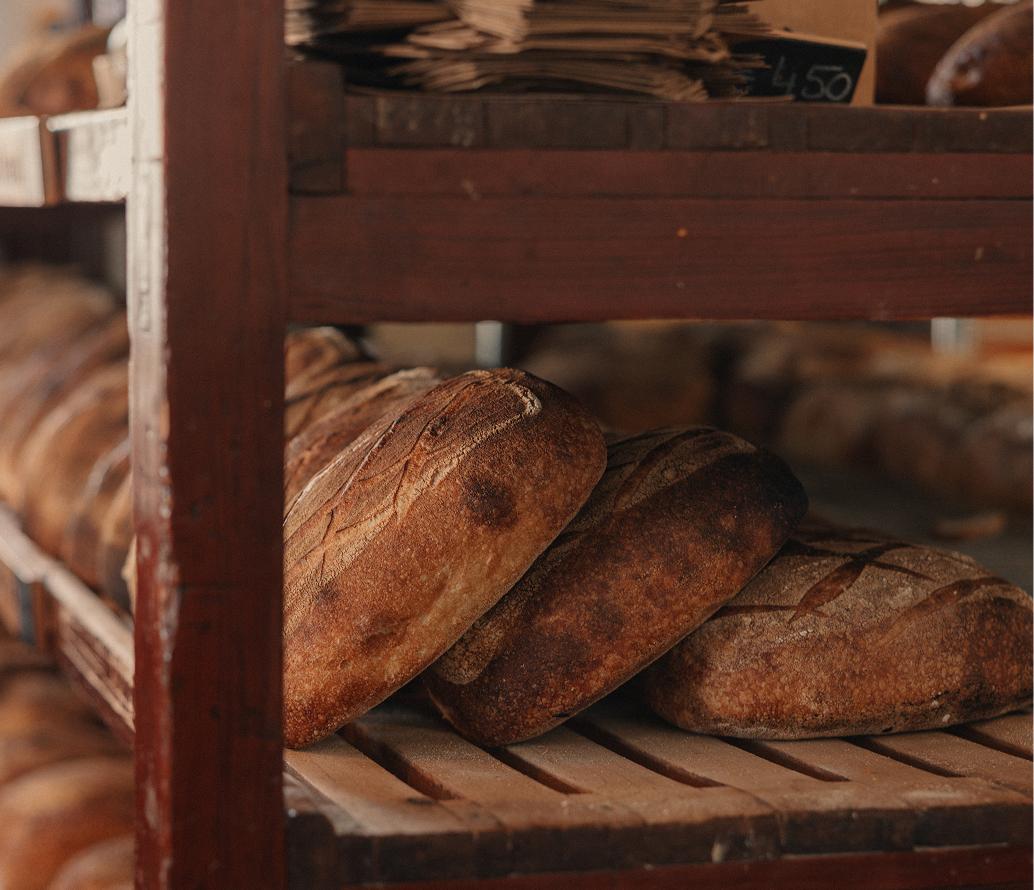 Rows of crusty, dark-baked sourdough loaves resting on rustic wooden bakery shelves with a chalked price tag above