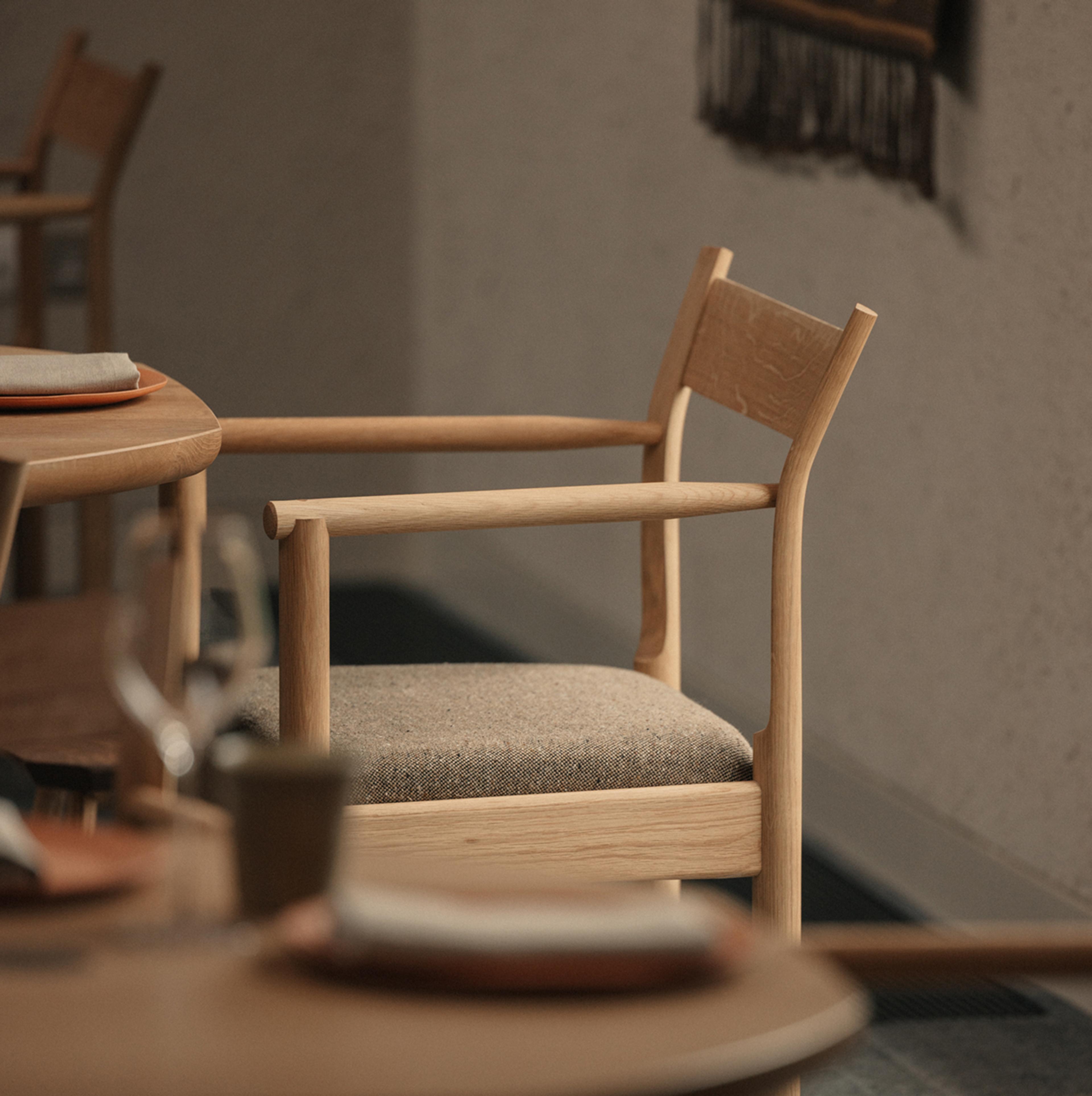 Oak dining chair with a woven wool seat beside round timber tables set with plates and linen napkins in the restaurant