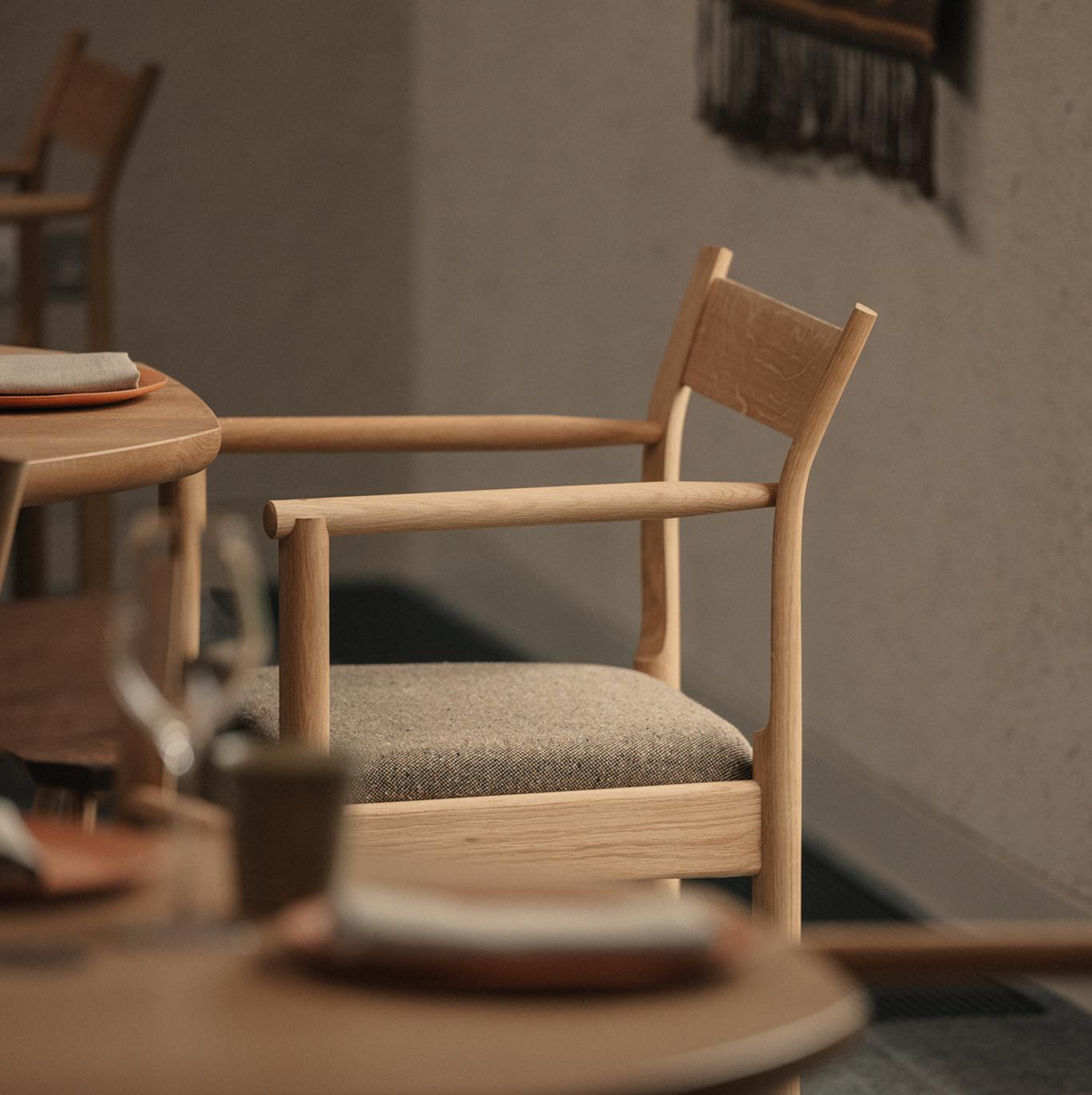 Oak dining chair with a woven wool seat beside round timber tables set with plates and linen napkins in the restaurant