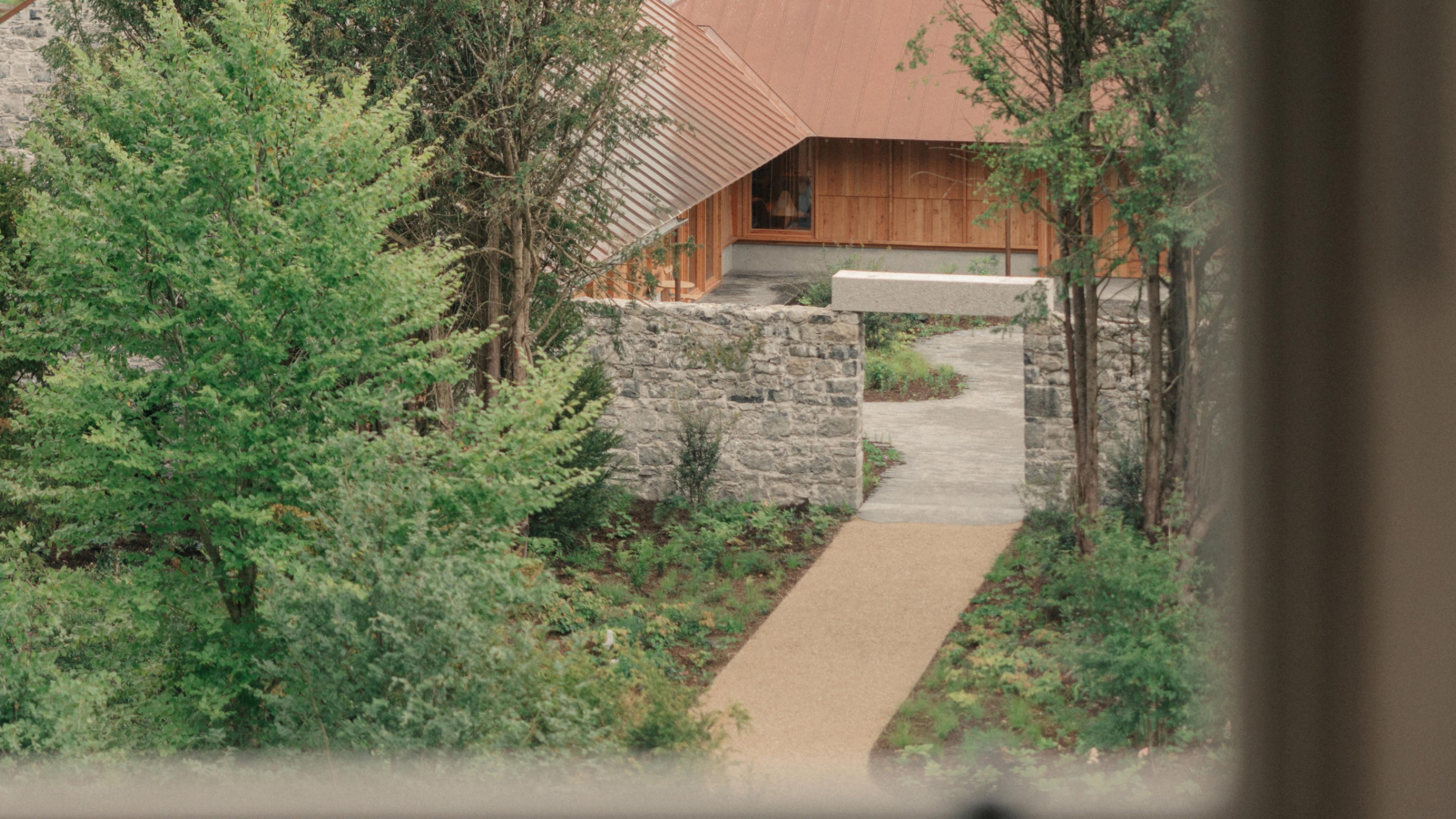 View from the Loft Suite window over a gravel path leading through a stone garden wall to the timber-clad, copper-roofed restaurant among trees