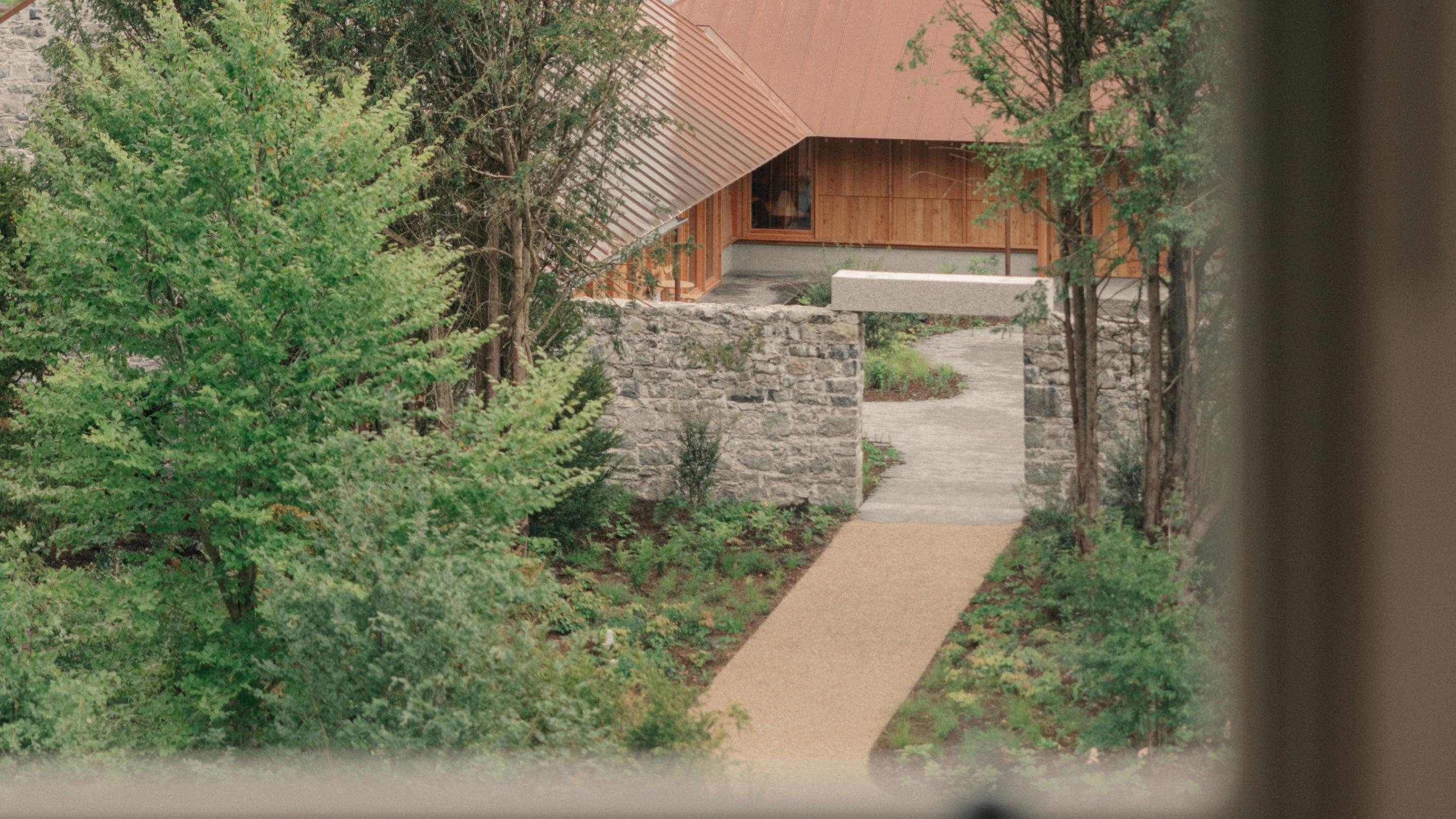 View from the Loft Suite window over a gravel path leading through a stone garden wall to the timber-clad, copper-roofed restaurant among trees