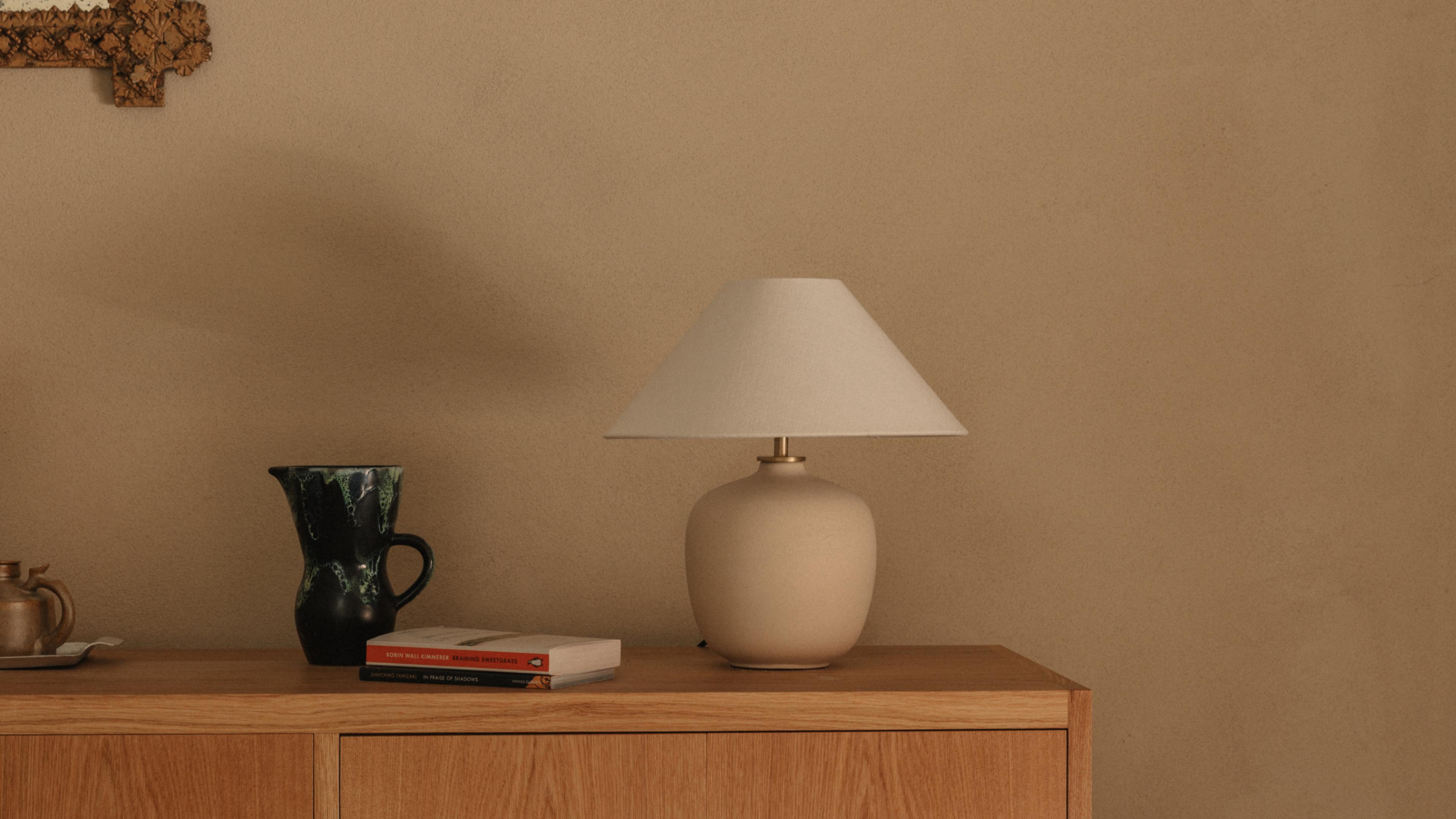 Cream ceramic lamp, dark green jug, books and a pewter teapot arranged on an oak sideboard in the Coachhouse Suite