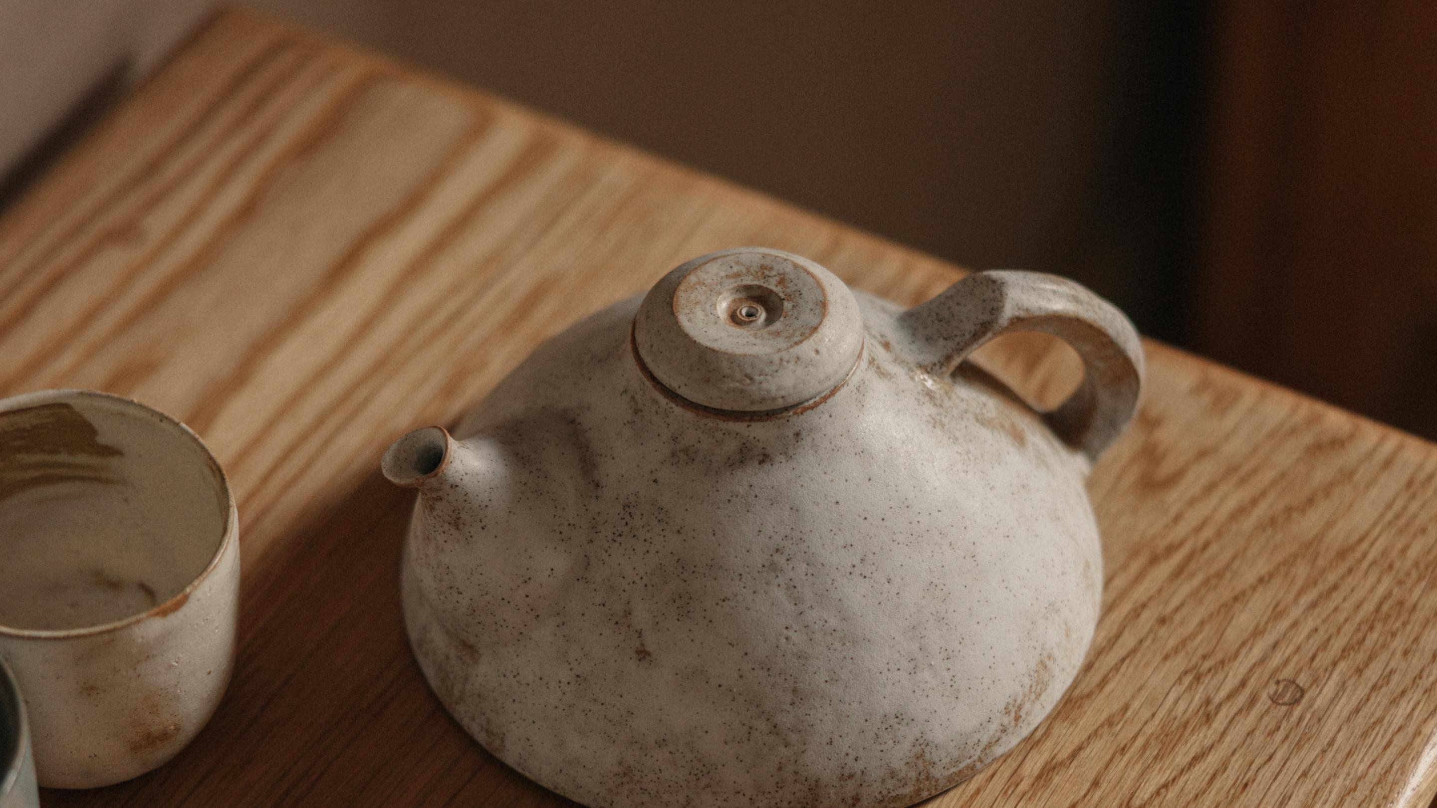 Hand-thrown speckled stoneware teapot and cup on a wooden table