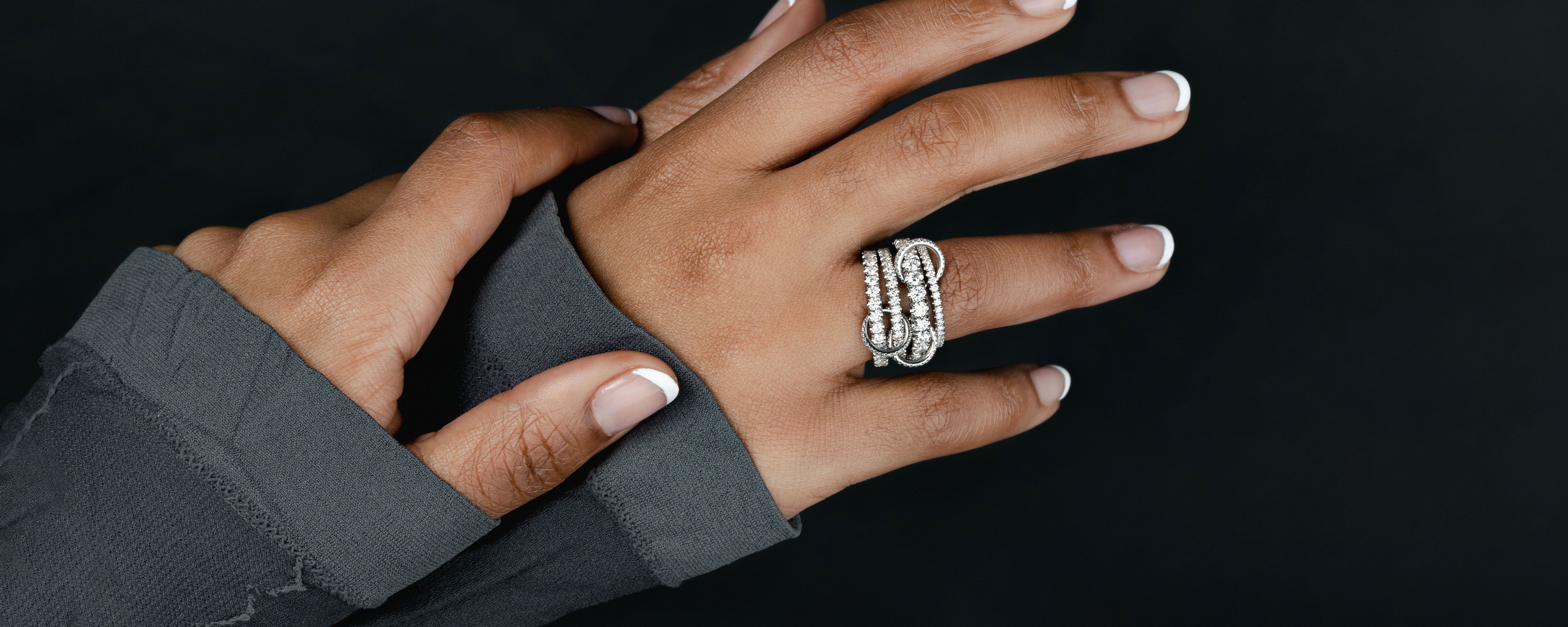 Spinelli Kilcollin image of mother and child's hands against white garment featuring linked rings stacked and spread across fingers, wearing single band, Polaris Blanc and Vela SG Shop in Stock for Mother's Day Luxury Jewelry made to order 