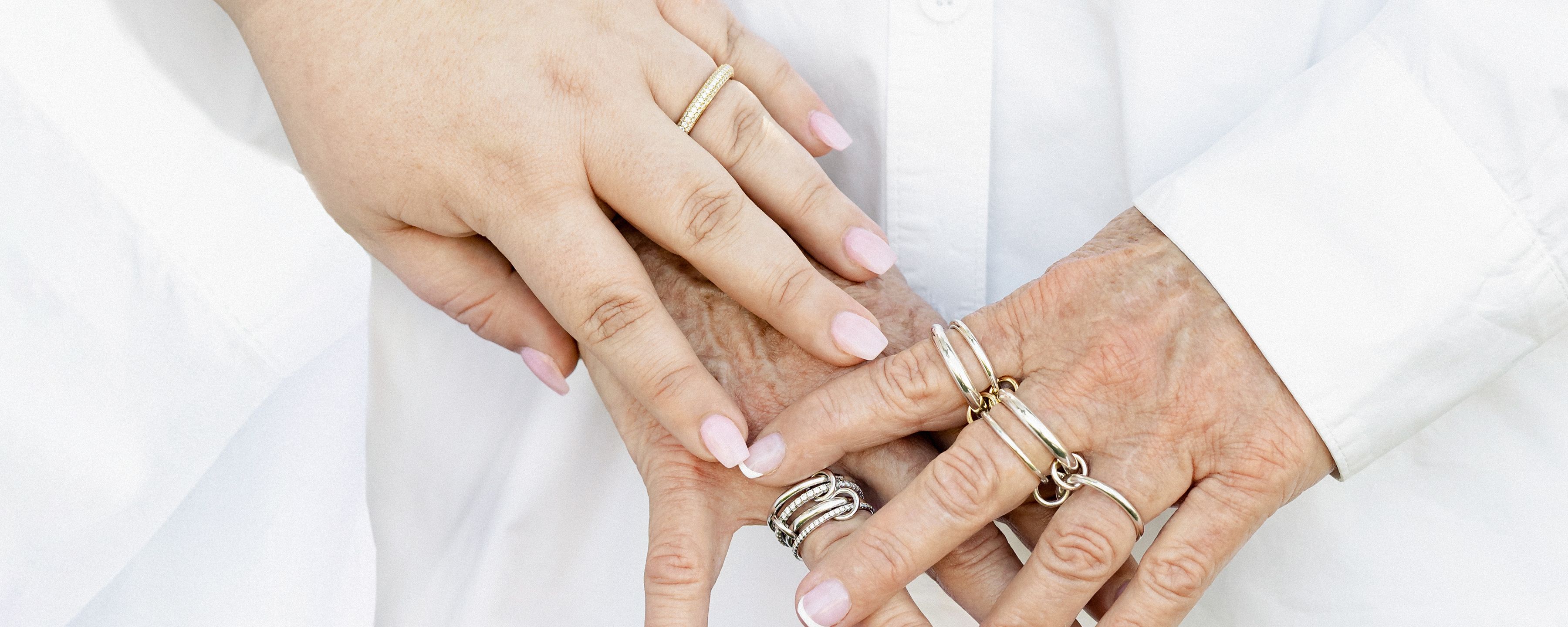 Spinelli Kilcollin image of mother and child's hands against white garment featuring linked rings stacked and spread across fingers, wearing single band, Polaris Blanc and Vela SG Shop in Stock for Mother's Day Luxury Jewelry made to order 