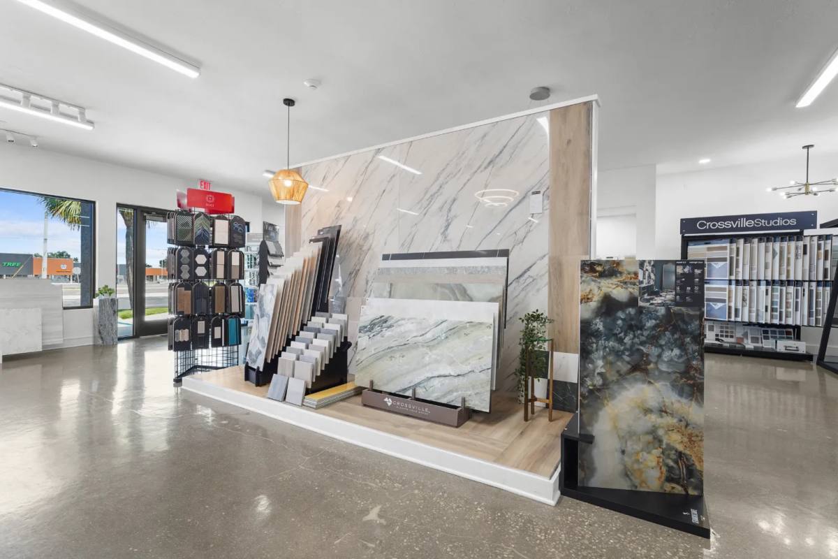 Showroom platform of large marble-look porcelain slabs and sample racks in front of a bookmatched slab wall, a Crossville Studios sample wall at right
