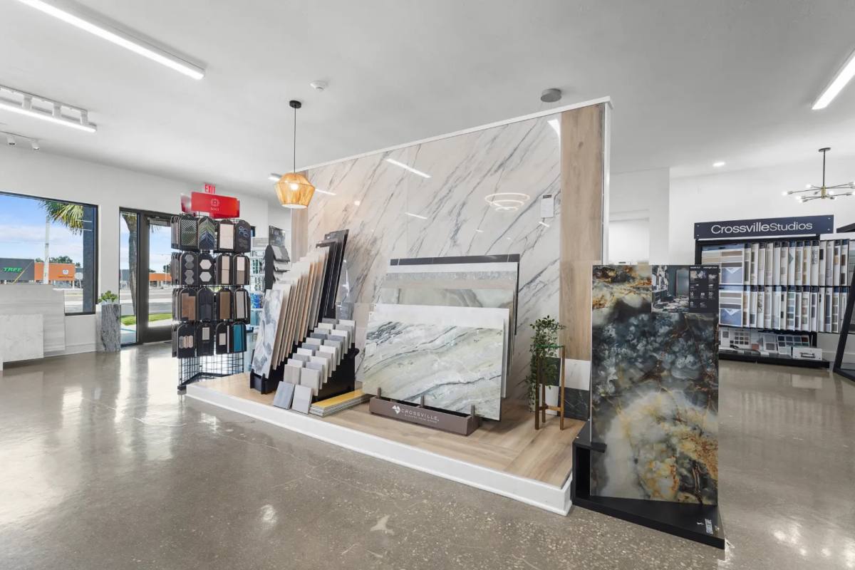 Showroom platform of large marble-look porcelain slabs and sample racks in front of a bookmatched slab wall, a Crossville Studios sample wall at right