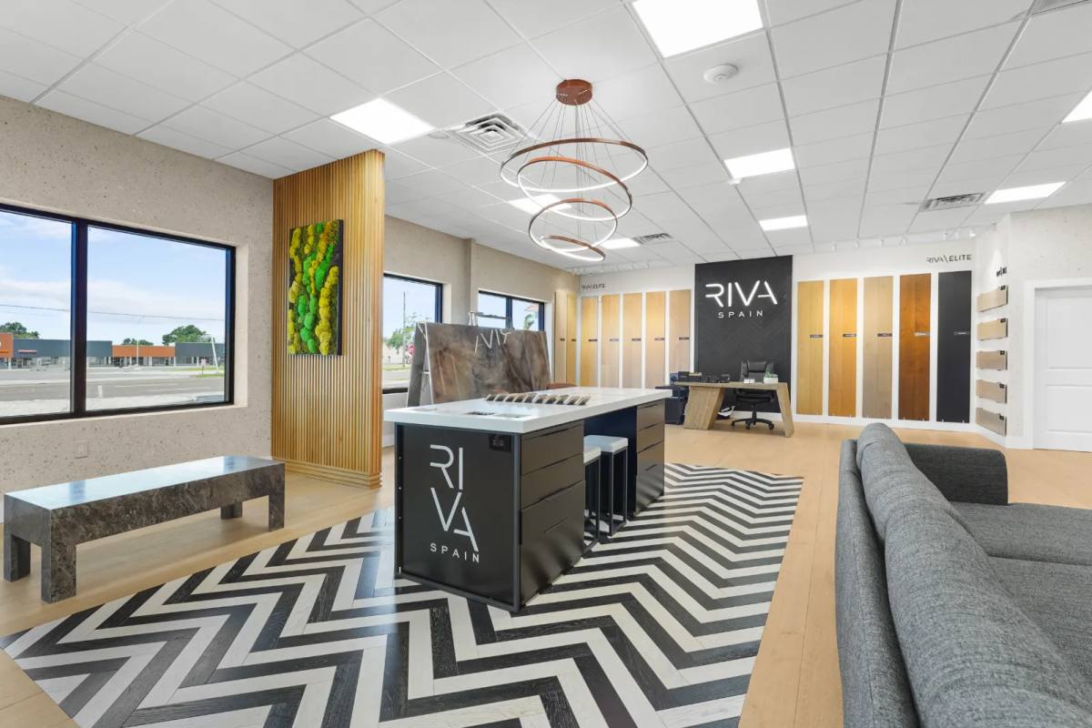 Flooring showroom with a black-and-white chevron floor, a black sample island under a ring chandelier, a moss panel on a slatted column and oak plank samples along the far wall