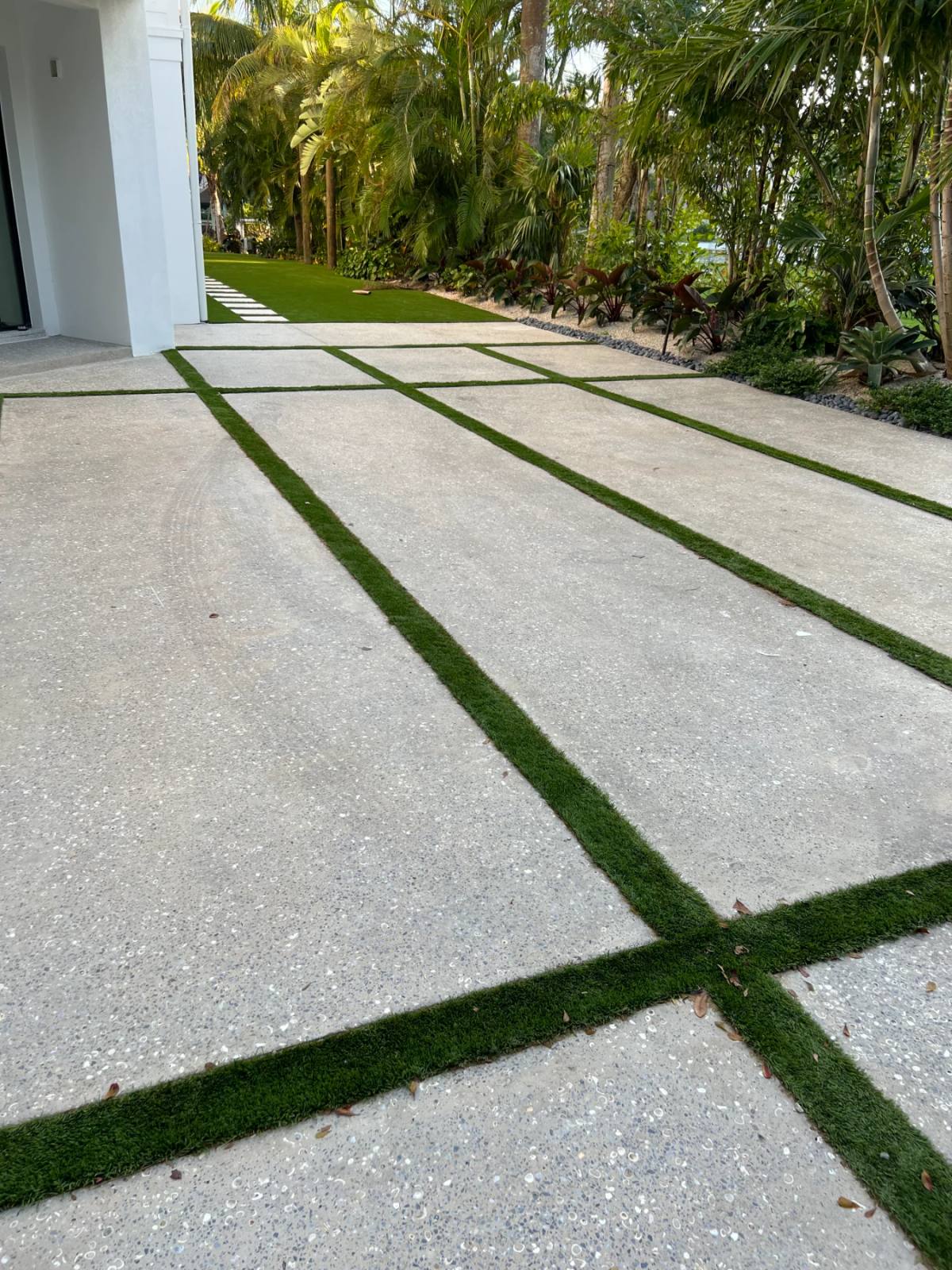 Motor court of large Shellcrete slabs separated by narrow strips of artificial turf, running past a white house