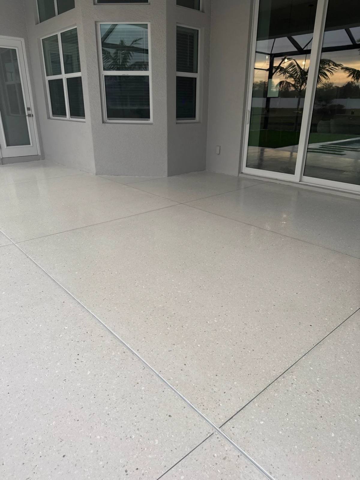 A covered lanai at dusk with a polished Shellcrete floor reflecting the sliding doors