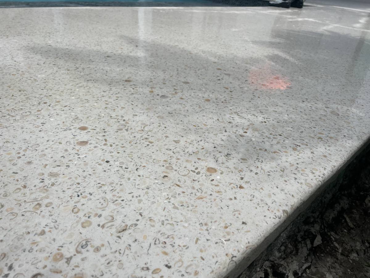 Wide close view along a wet polished Shellcrete pool coping, the surface still dark from water