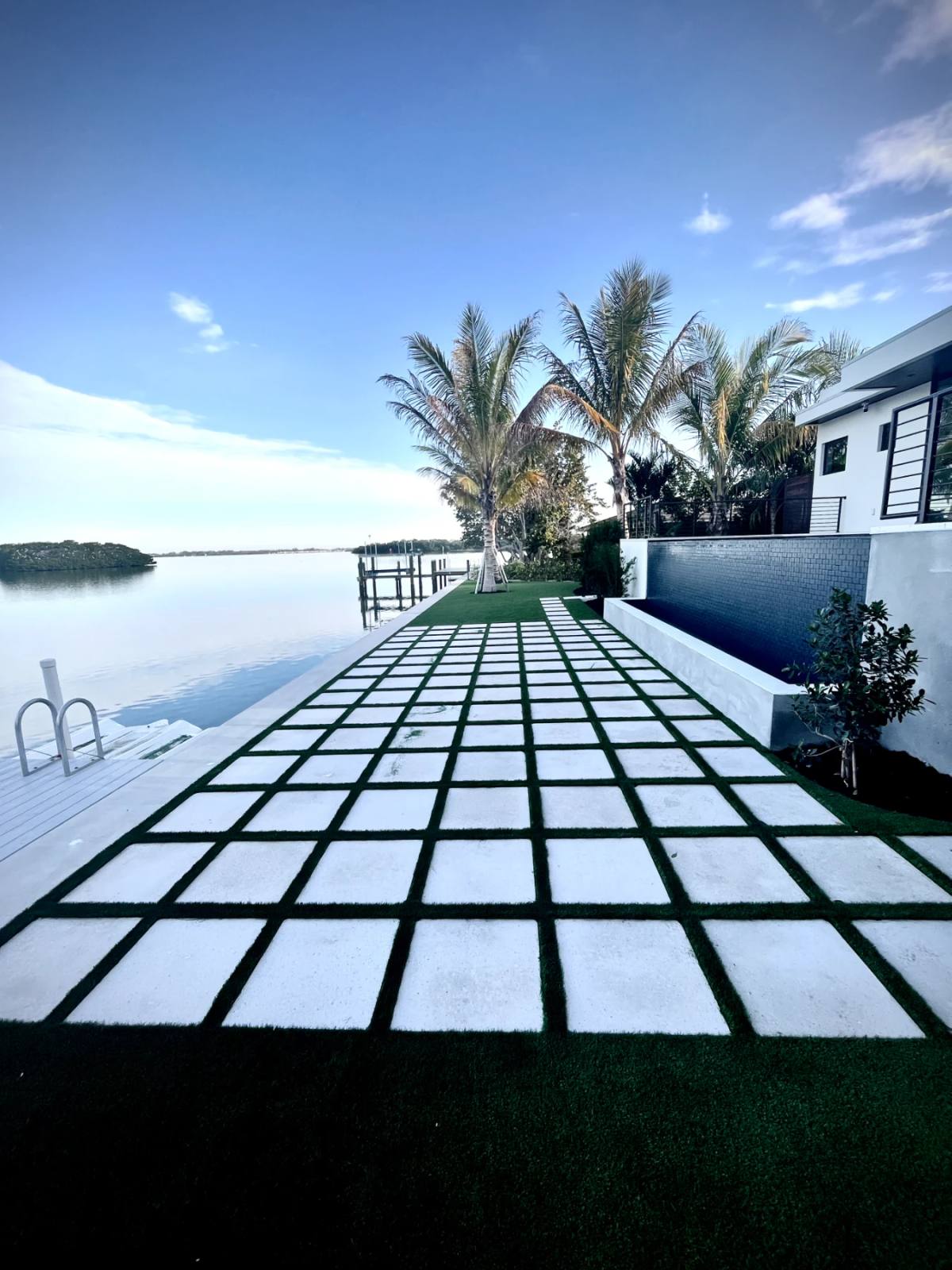 Checkerboard of white Shellcrete squares set into artificial turf running to a waterfront dock at dusk