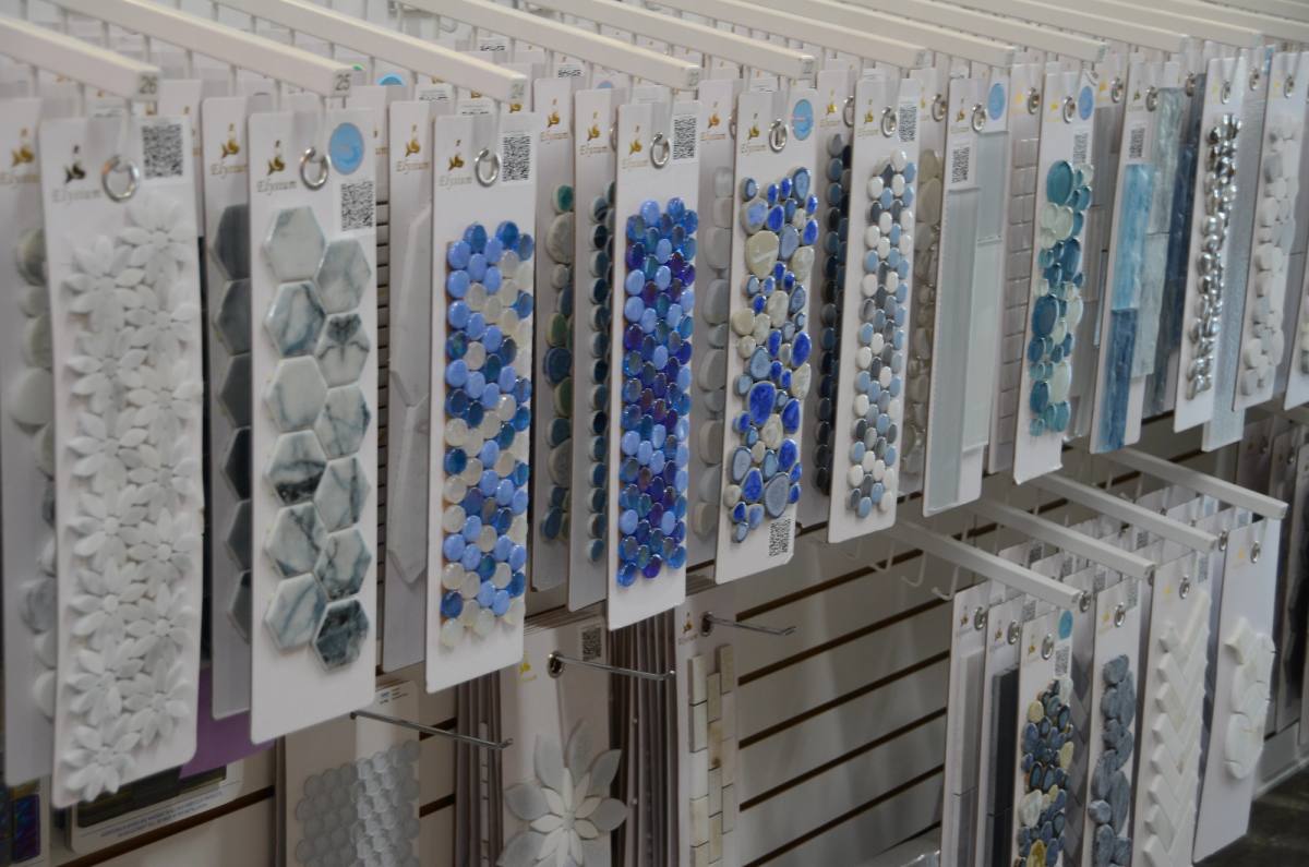 Vertical mosaic sample strips hung in rows — blue glass, white marble and stone mosaics