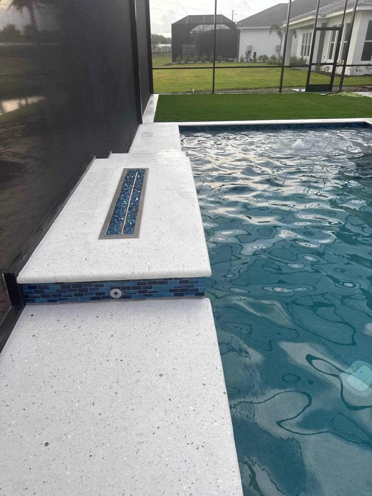 A screened pool with a Shellcrete deck and a raised ledge holding a linear fire feature
