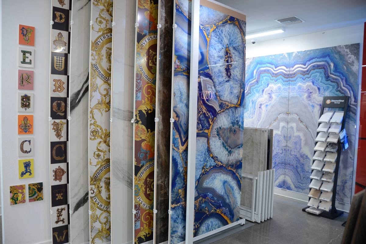Full-height backlit blue agate slabs and gold-veined panels on the showroom's display wall, beside a grid of patterned art tiles