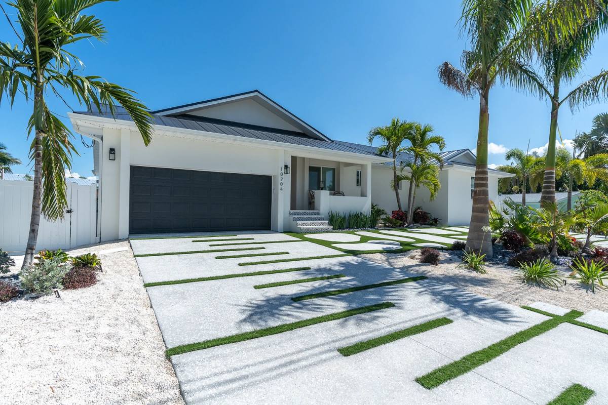 A low white coastal house behind a poured shellcrete driveway with turf strips set into it, palms across the front