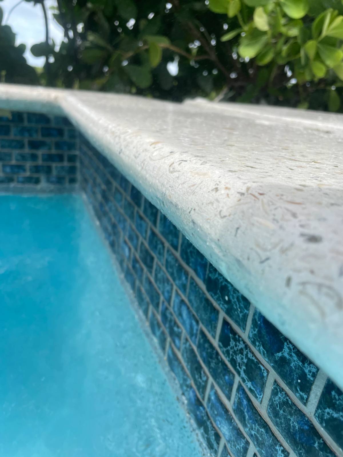 Shellcrete pool coping along its length above brick-pattern blue-green mosaic and turquoise water