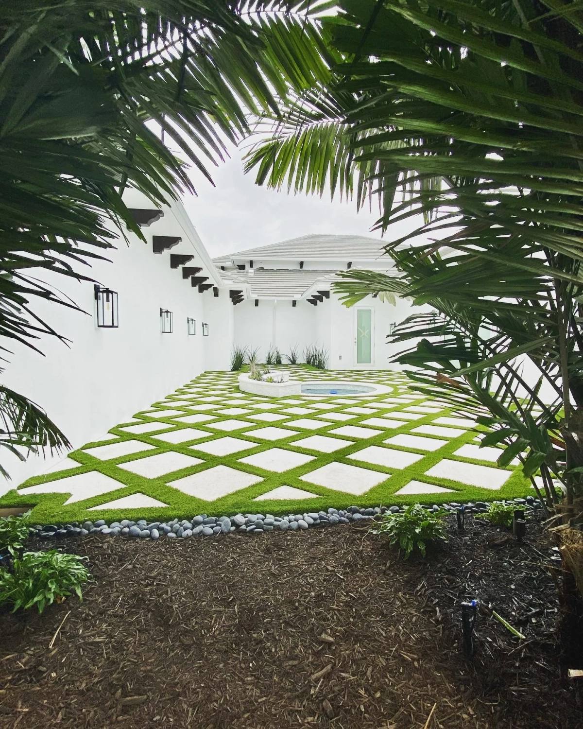 Courtyard paved in white Shellcrete diamonds with turf joints, framed by palms and leading to a round spa