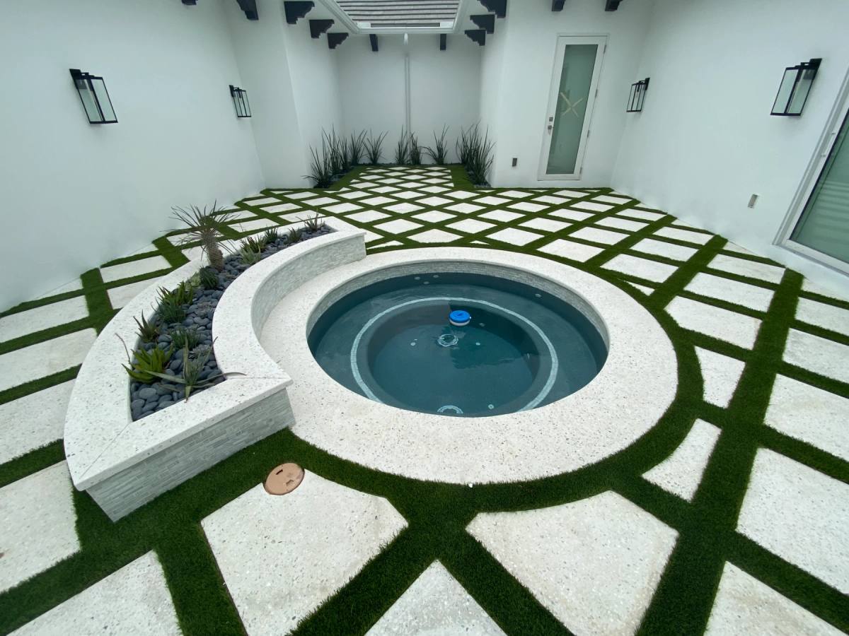 A courtyard of Shellcrete slabs and turf set on a diamond grid around a round spa