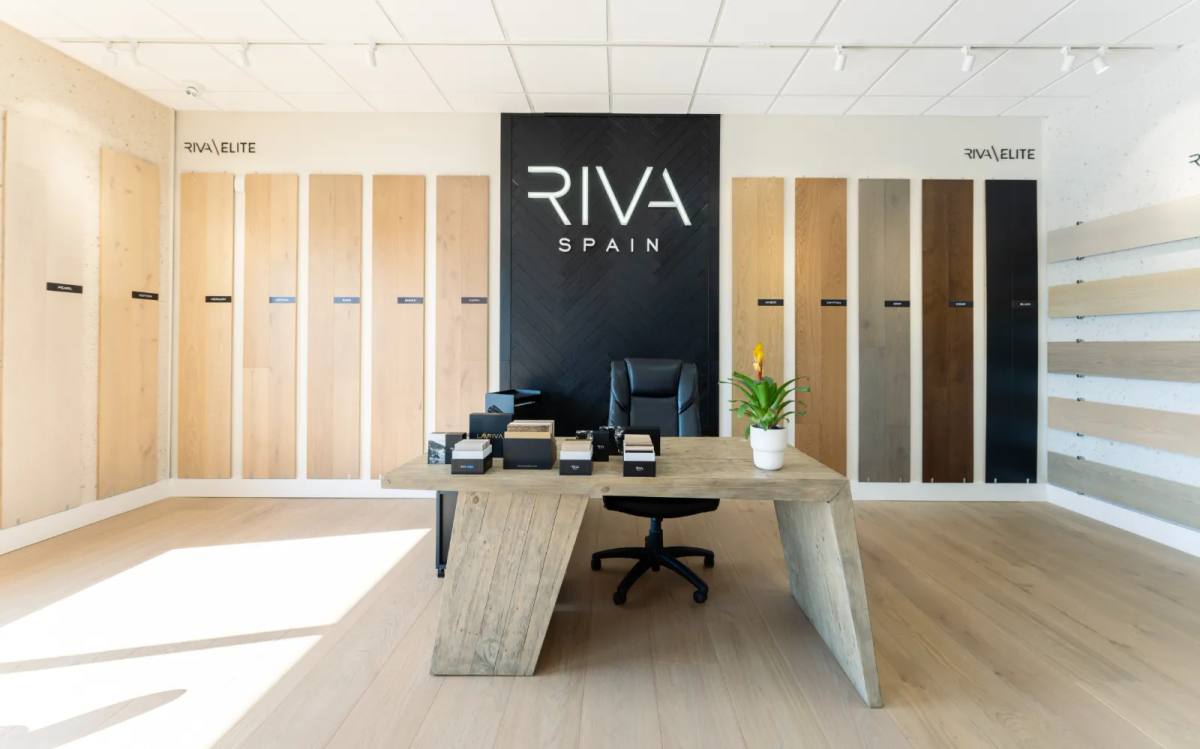 A reclaimed-wood consultation table in front of a black feature wall with a backlit sign, oak plank sample walls running off to both sides