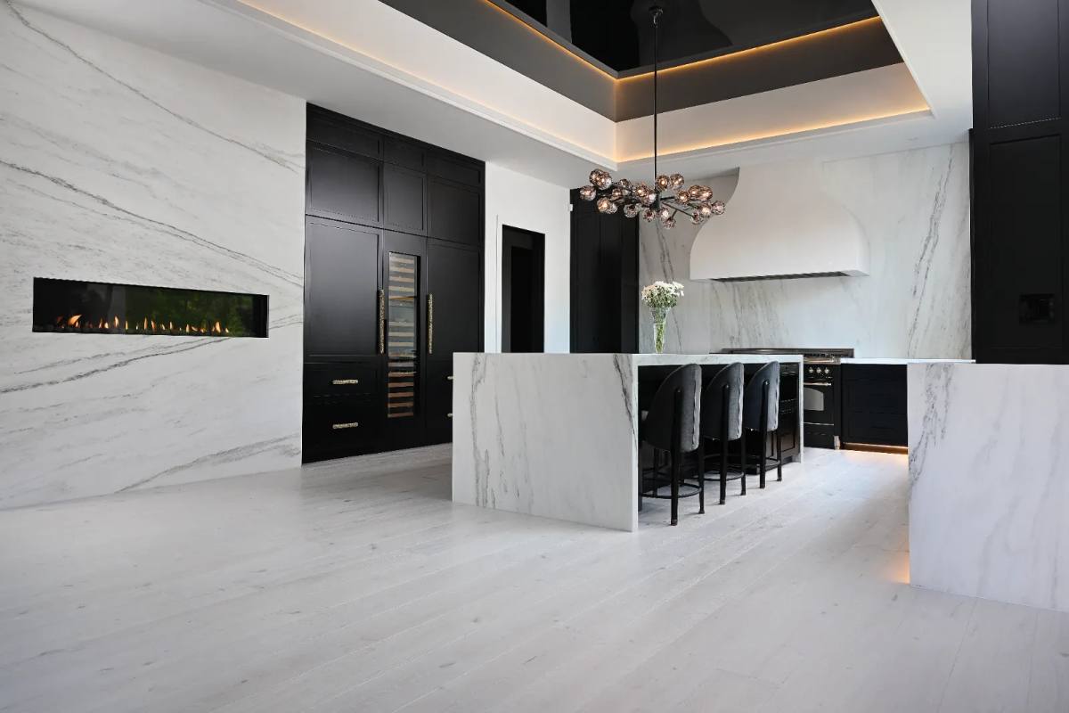 Black-and-white kitchen with book-matched marble slab walls, a marble waterfall island, a linear gas fireplace and whitewashed plank floors
