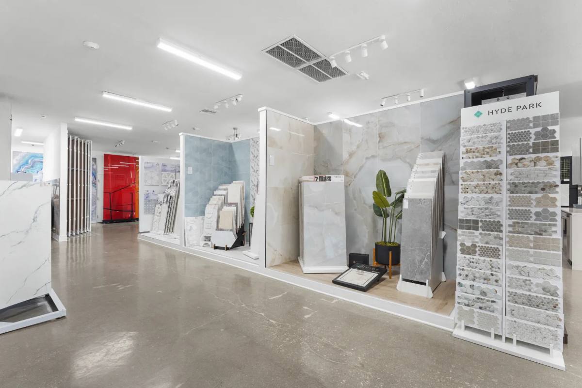 Showroom aisle of marble-look porcelain panels, a pale blue tile wall and a Hyde Park mosaic tower, on a polished concrete floor