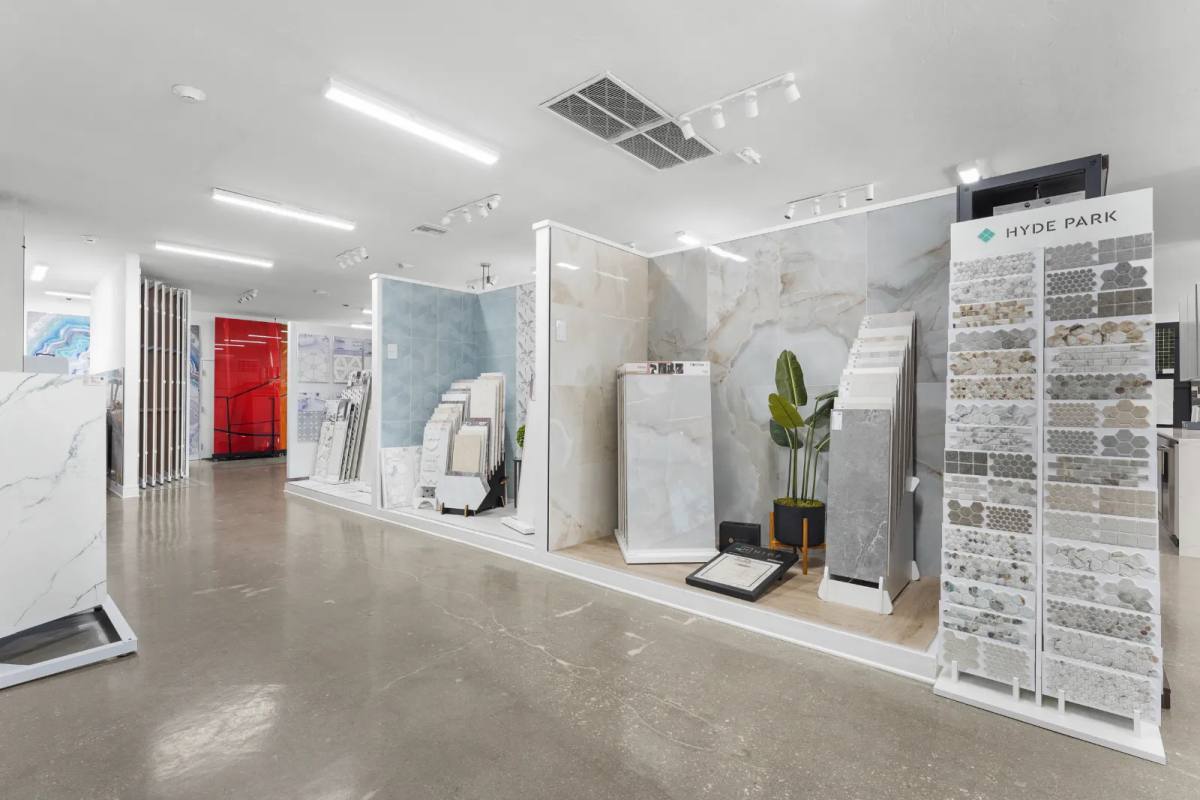 Showroom aisle of marble-look porcelain panels, a pale blue tile wall and a Hyde Park mosaic tower, on a polished concrete floor