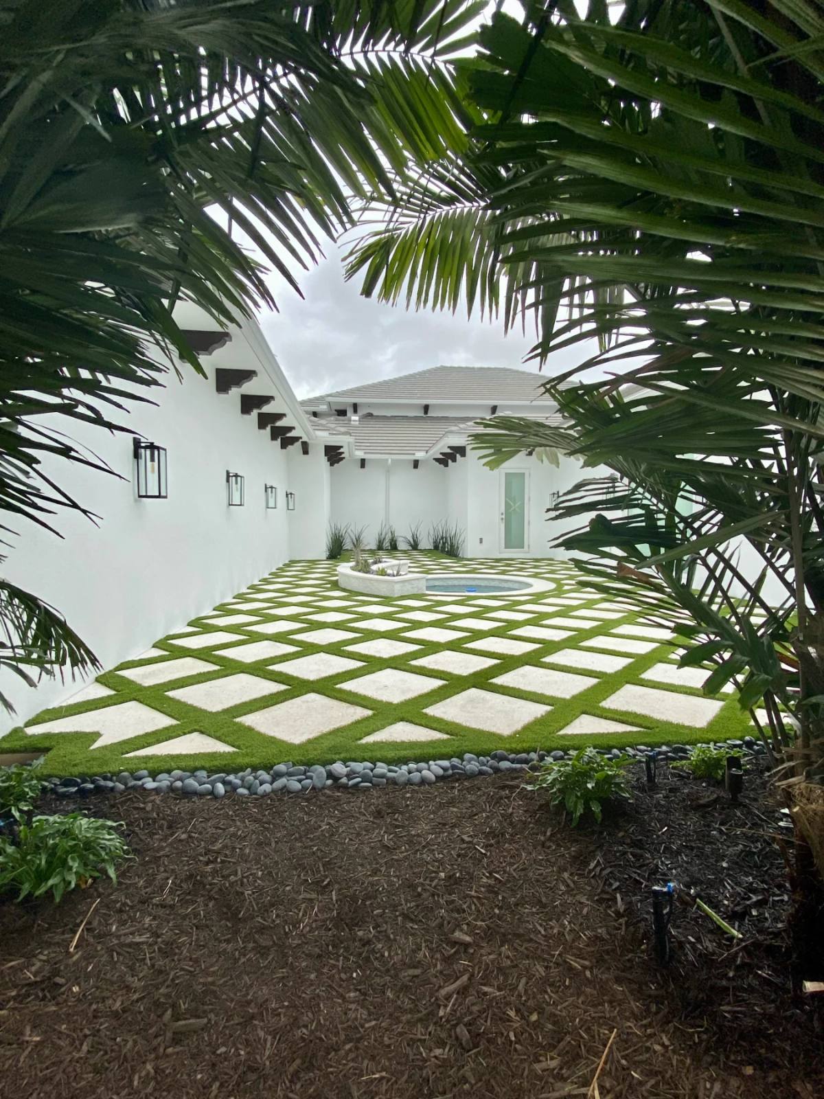 Enclosed white courtyard with a diamond grid of Shellcrete slabs set in artificial turf running to a round spa