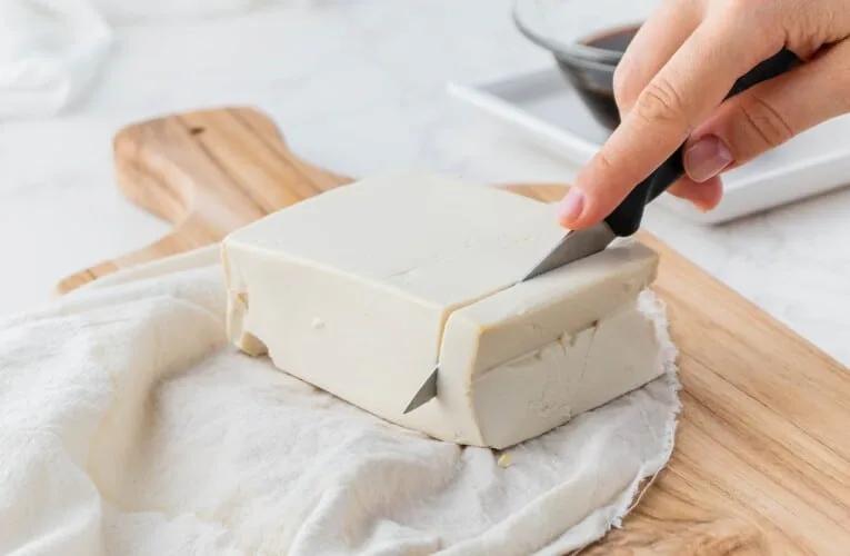 Delicious Tofu Recipe|Woman slicing tofu on wooden chopping board.