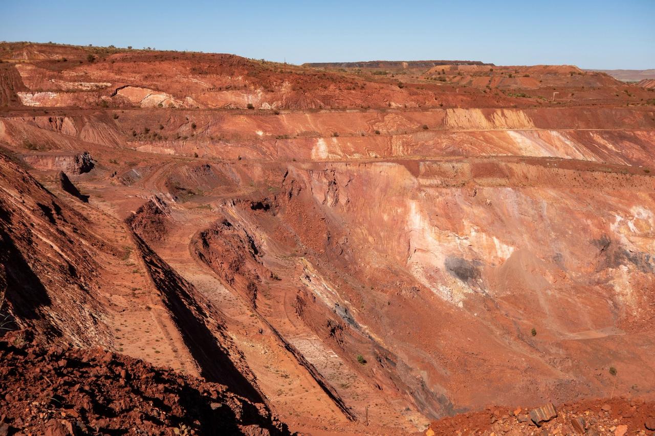 Active deep pit of red iron ore mine in Pilbara region in Western Australia with shadows of various levels.