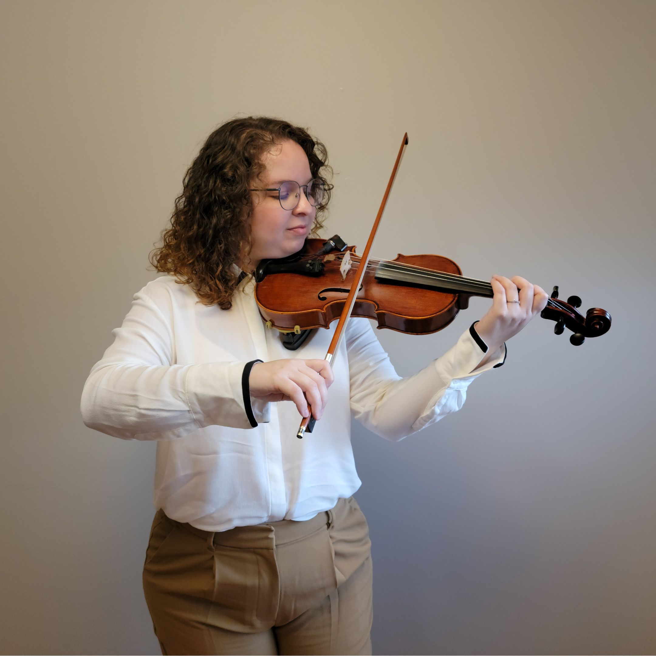 Young woman with curly hair and glasses plays violin