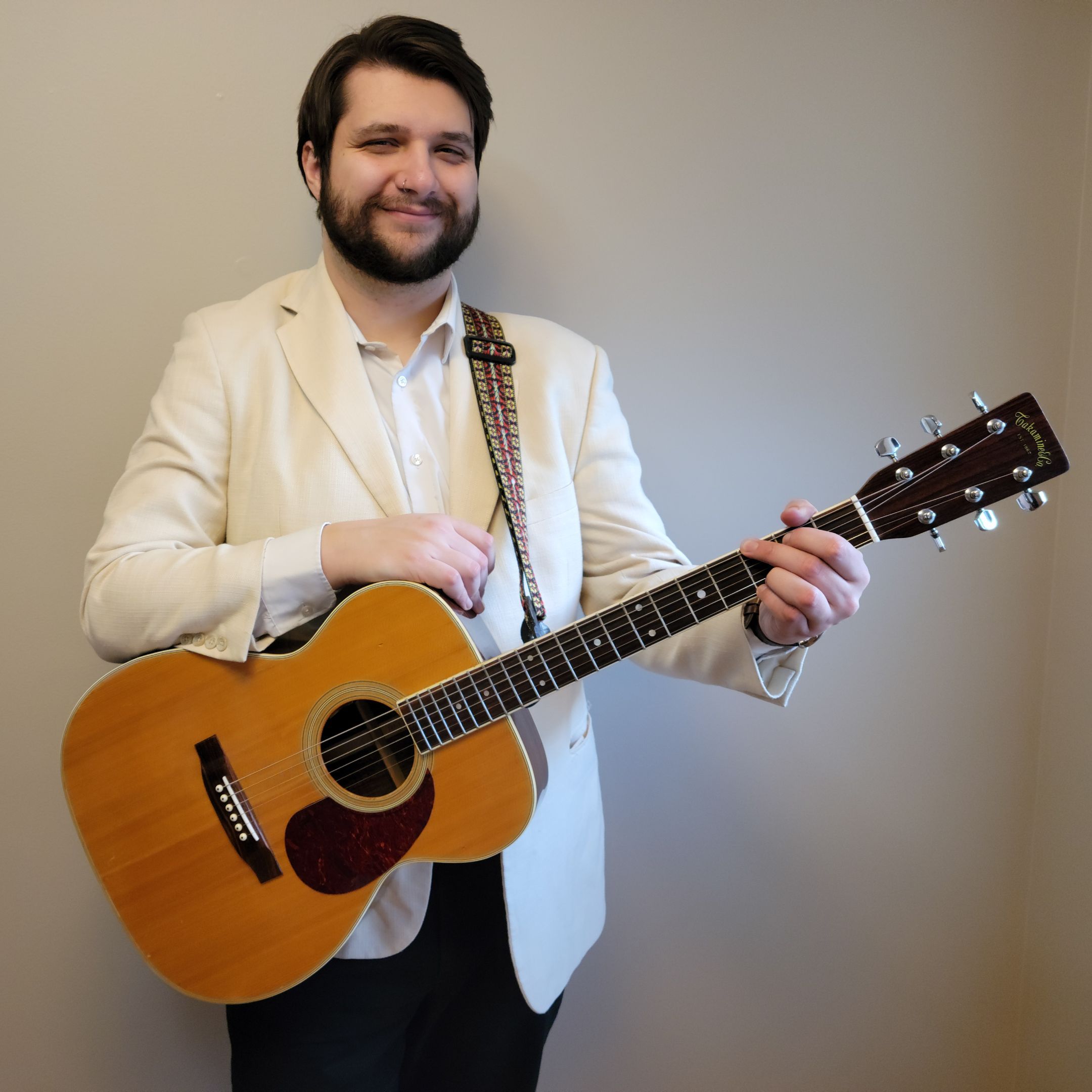 Man in blazer holds G chord on guitar while smiling at camera