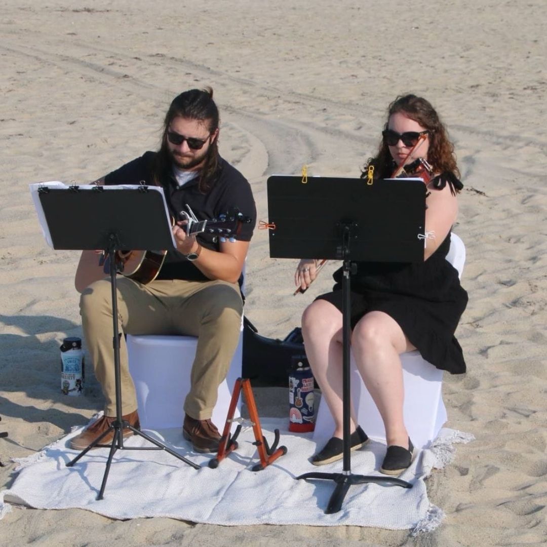 Man and woman play instruments on beach for wedding