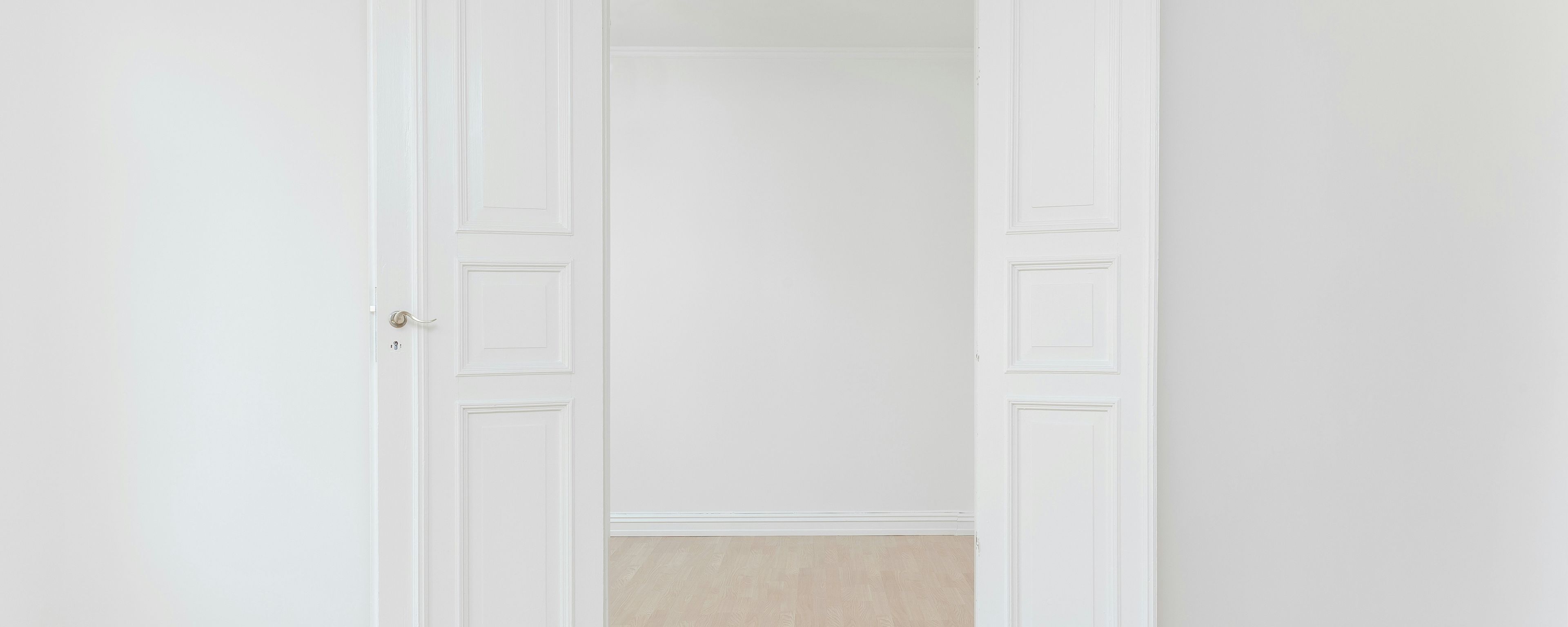 an empty room with white walls and wooden floors and two white doors open .