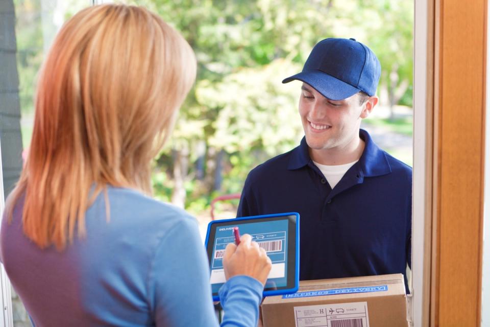 Delivery driver smiling as a customer signs for a package on a digital tablet at the doorstep