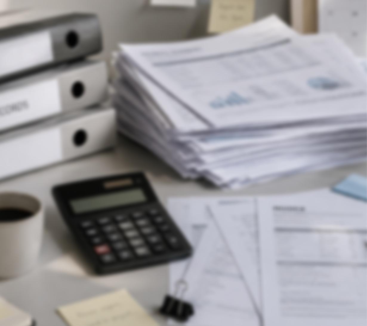 Desk piled with printed reports and a calculator