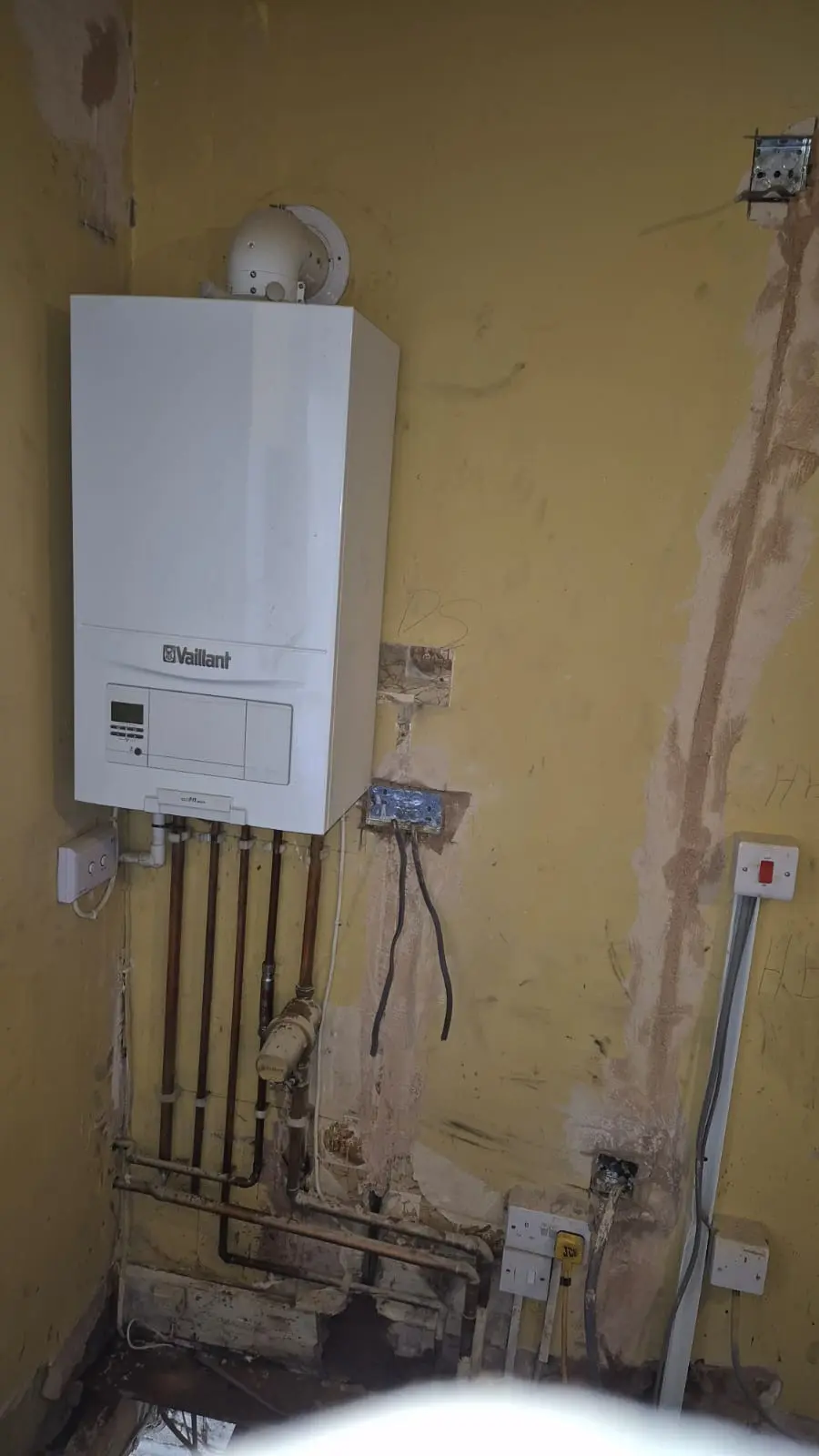 The original boiler position after removal, showing the flue hole and capped pipework