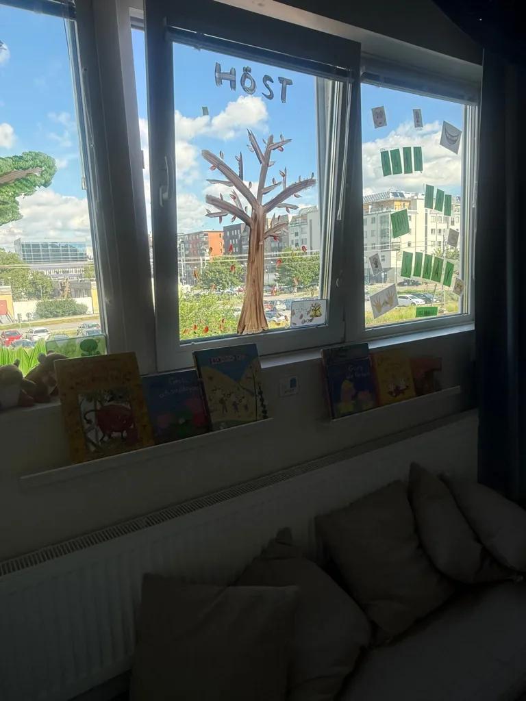 Höstträd målat på fönstret ovanför läshörnans böcker