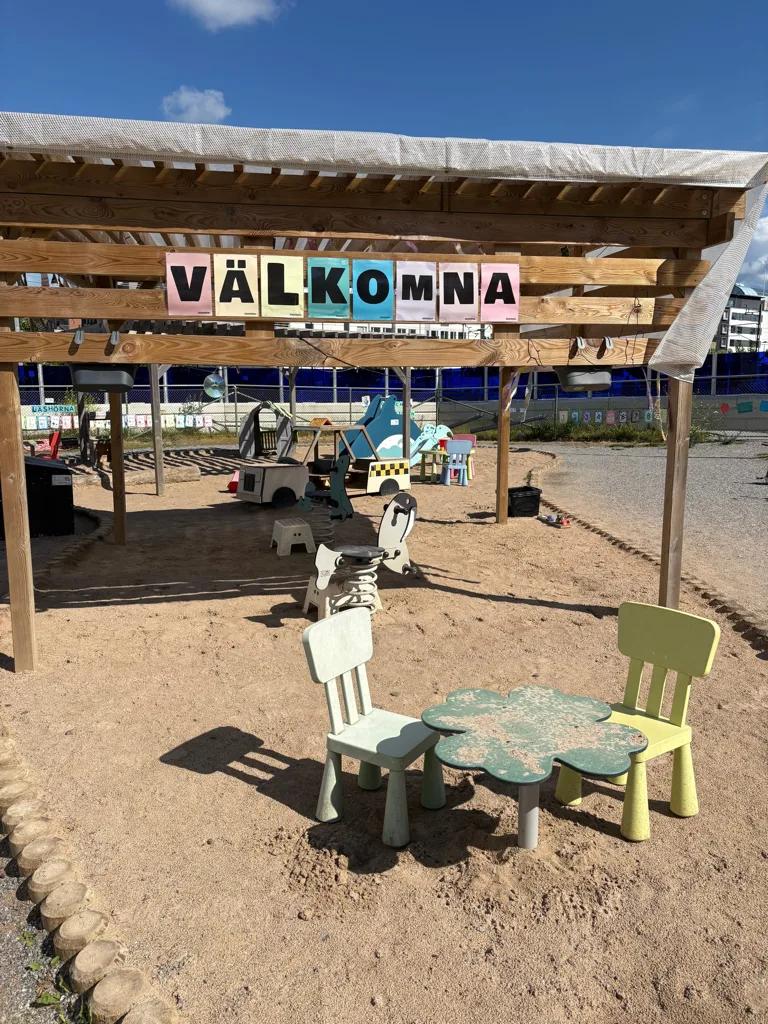 Välkomna-skylt över pergolan vid sandlådan på gården